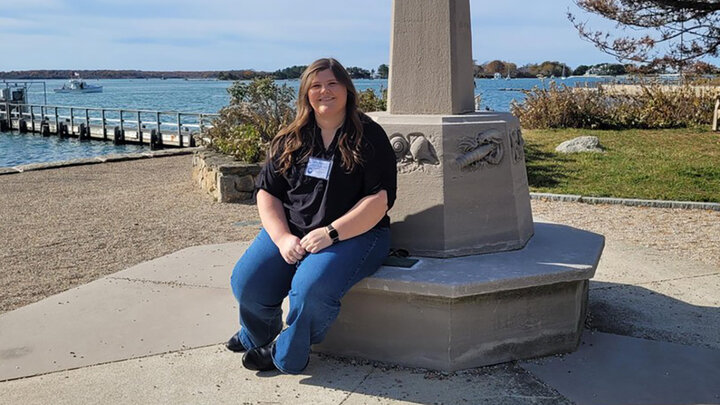 Kierstin Blomberg is photographed on a concrete bench near a lake.